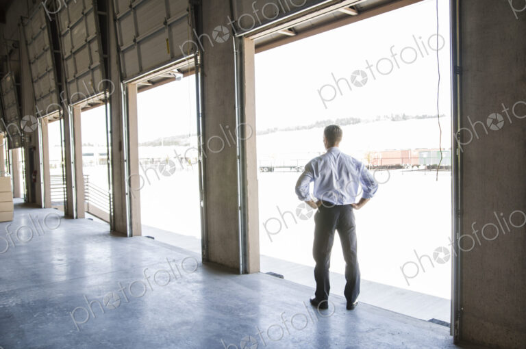 Caucasian man in shirt and tie standing in loading dock door of new empty warehouse…