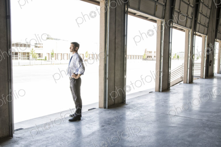 Caucasian man in shirt and tie standing in loading dock door of new empty warehouse…