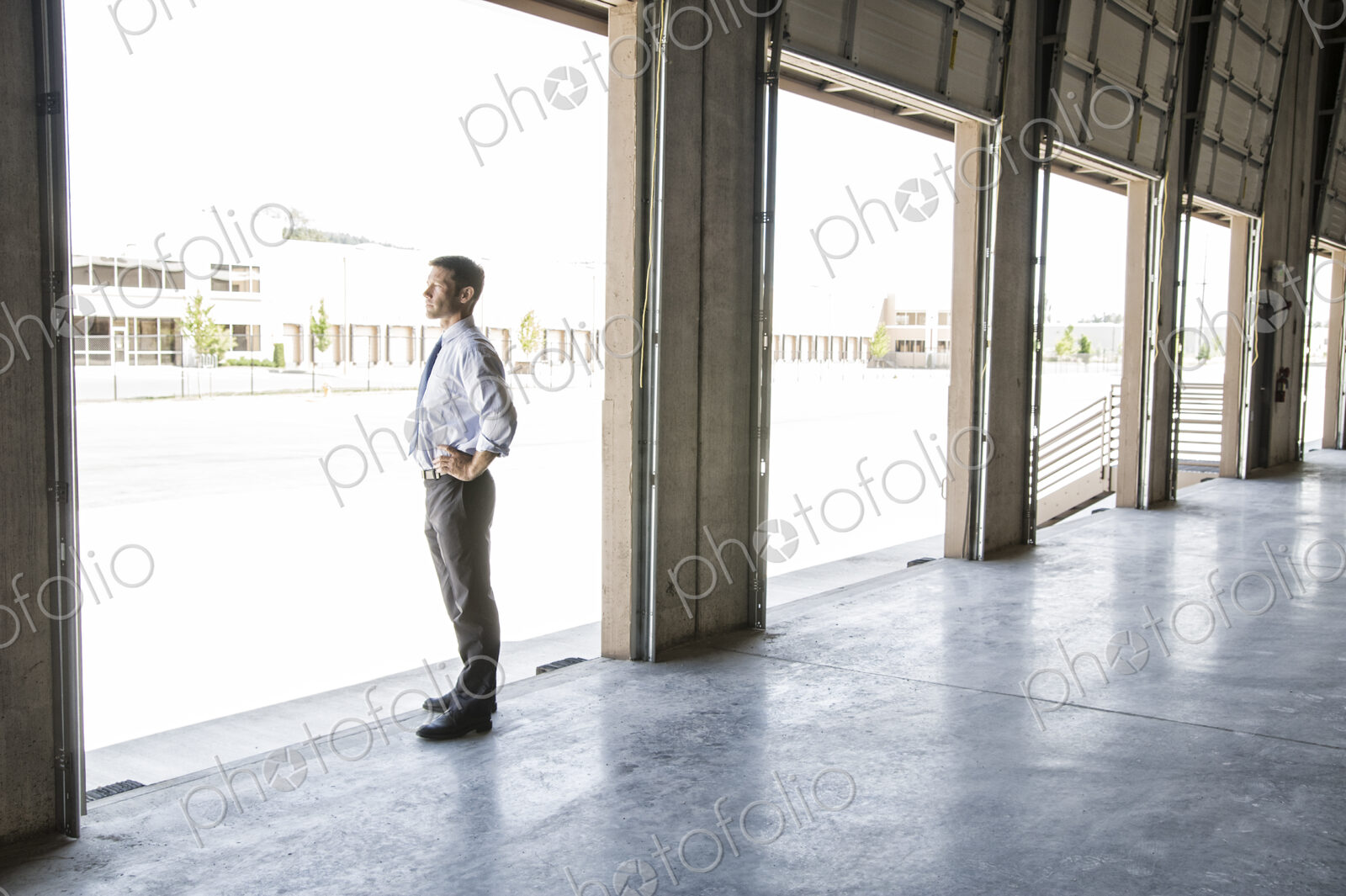 Caucasian man in shirt and tie standing in loading dock door of new empty warehouse…
