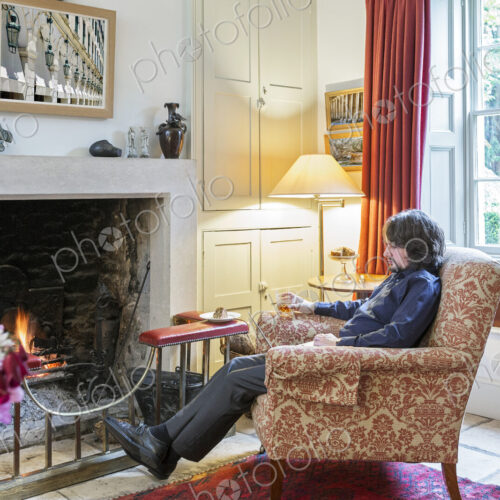 Caucasian man sitting in armchair near fireplace drinking cocktail