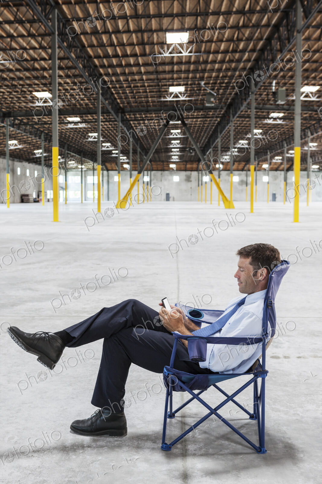 Caucasian man sitting in the middle of a new empty warehouse and using cell phone.