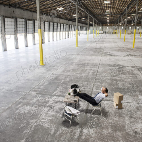 Caucasian man sitting with feet up on desk in front of loading dock doors in a new… Caucasian man sitting with feet up on desk in front of loading dock doors in a new…