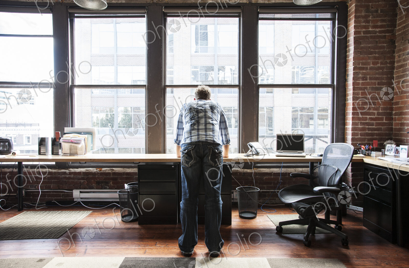 Caucasian man standing near a bank of windows at his creative office workstation.