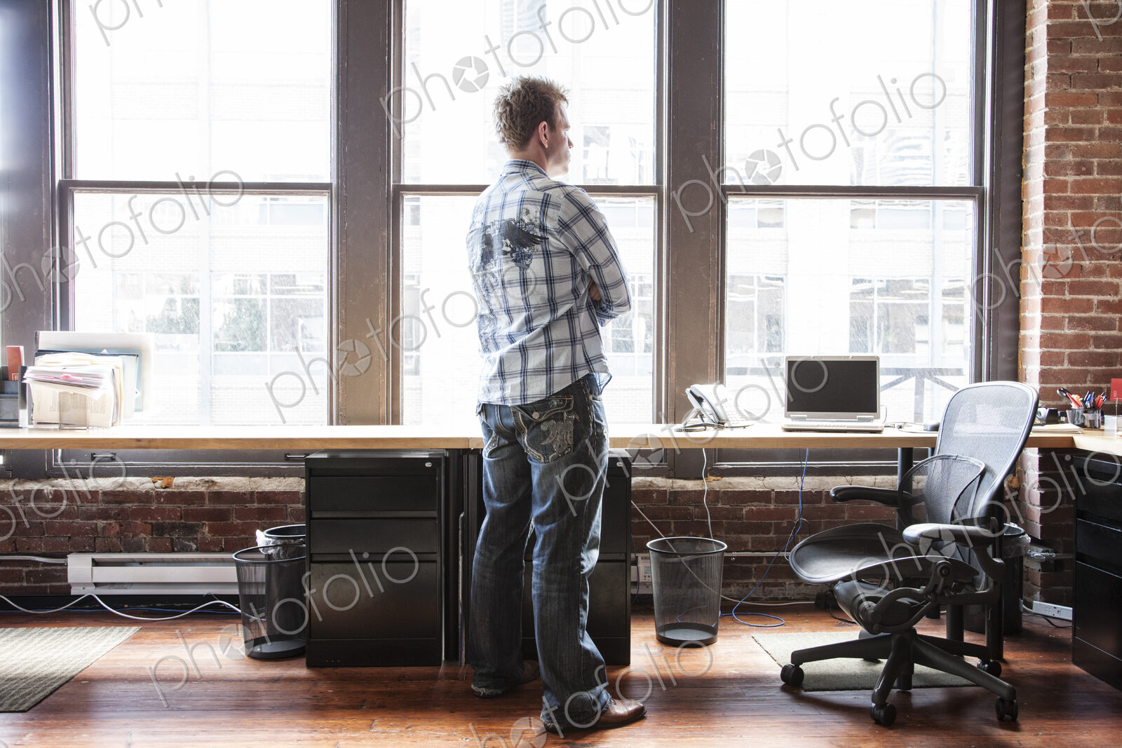 Caucasian man standing near a bank of windows at his creative office workstation.