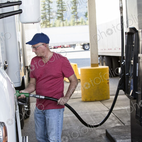 Caucasian man truck driver putting diesel fuel in his truck at a truck stop. Caucasian man truck driver putting diesel fuel in his truck at a truck stop.