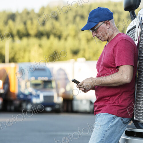 Caucasian man truck driver texting while standing next to the grill of his commercial… Caucasian man truck driver texting while standing next to the grill of his commercial…