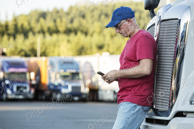Caucasian man truck driver texting while standing next to the grill of his commercial…