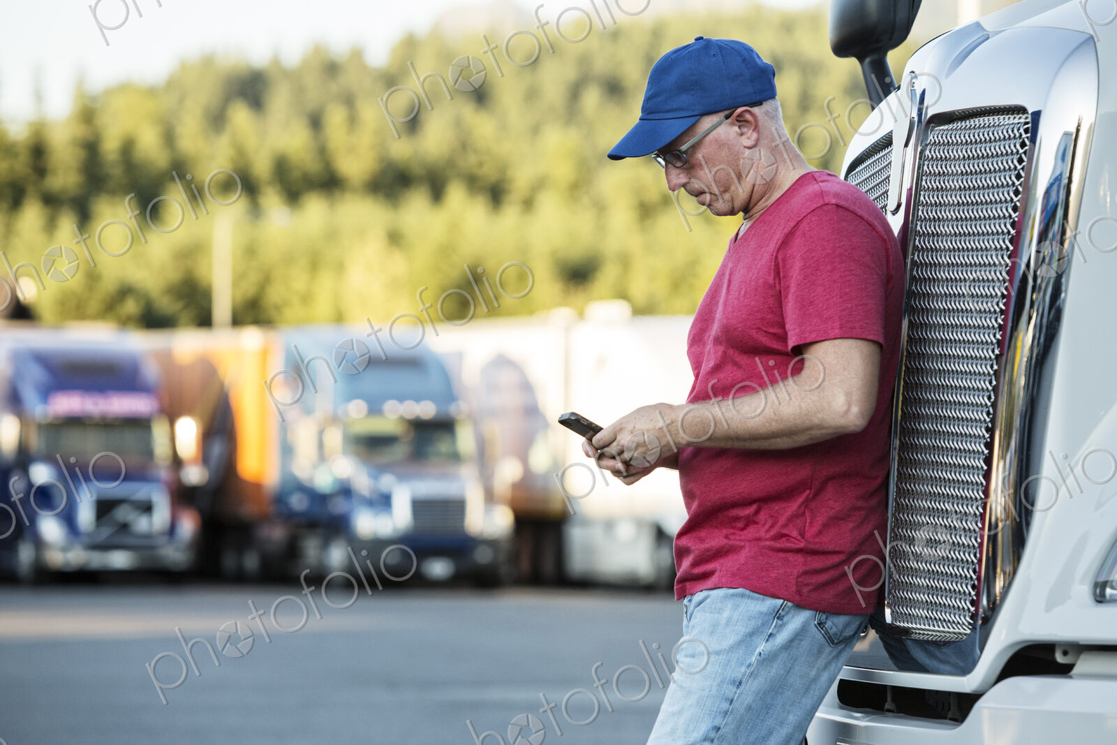 Caucasian man truck driver texting while standing next to the grill of his commercial…