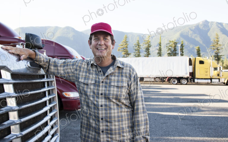 Caucasian man truck driver with his truck parked in a lot at a truck stop.