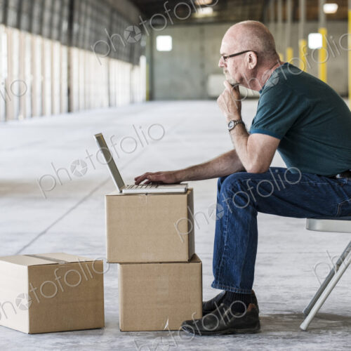 Caucasian man using boxes as desk and working on lap top computer in front of loading… Caucasian man using boxes as desk and working on lap top computer in front of loading…
