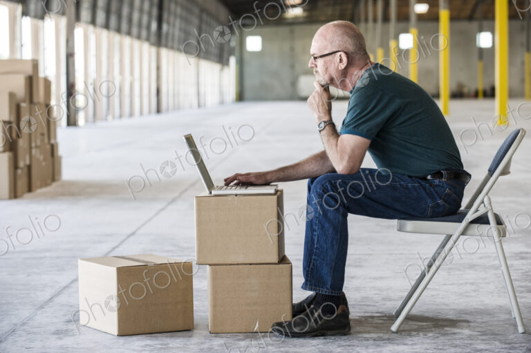Caucasian man using boxes as desk and working on lap top computer in front of loading…