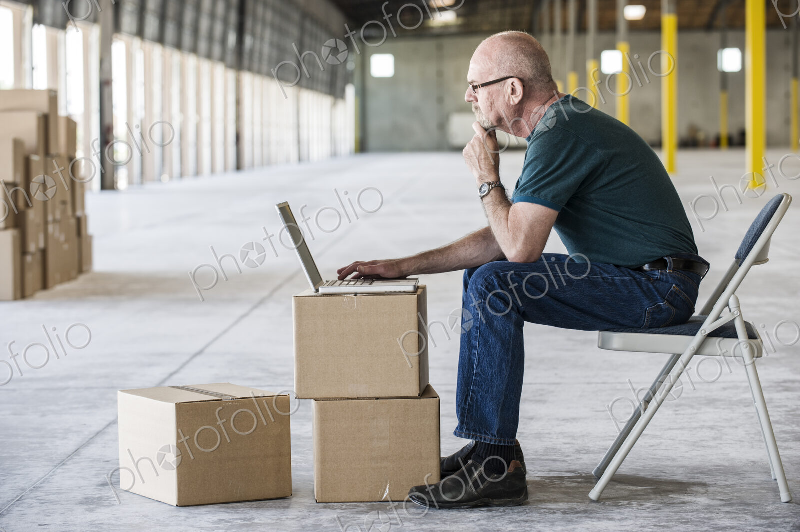 Caucasian man using boxes as desk and working on lap top computer in front of loading…