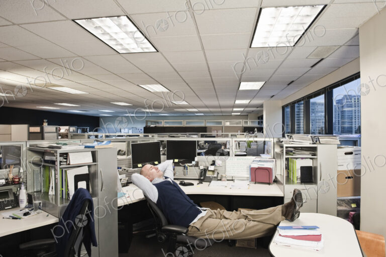 Caucasian man with his feet up on his desk sitting alone at his cubicle desk.