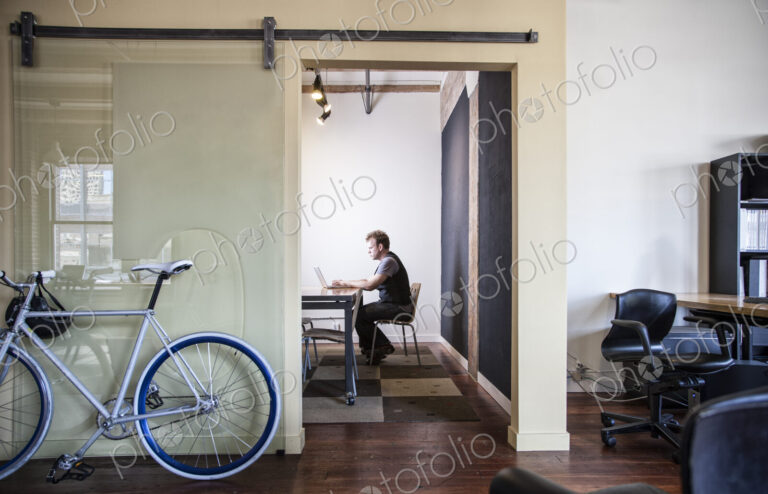 Caucasian man working at a laptop computer in a small conference room.