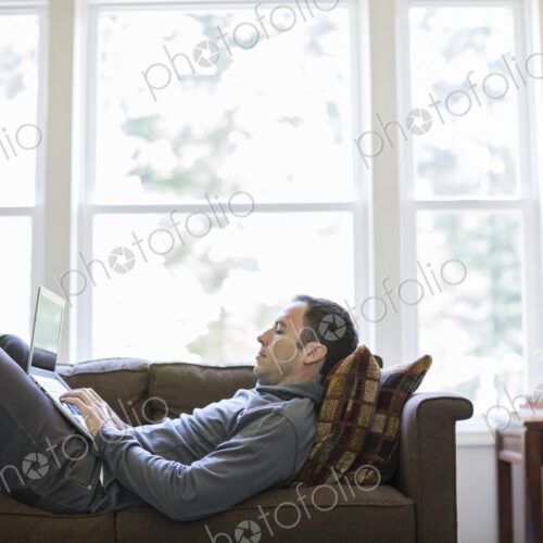 Caucasian man working on a laptop while on a couch in his home. Caucasian man working on a laptop while on a couch in his home.
