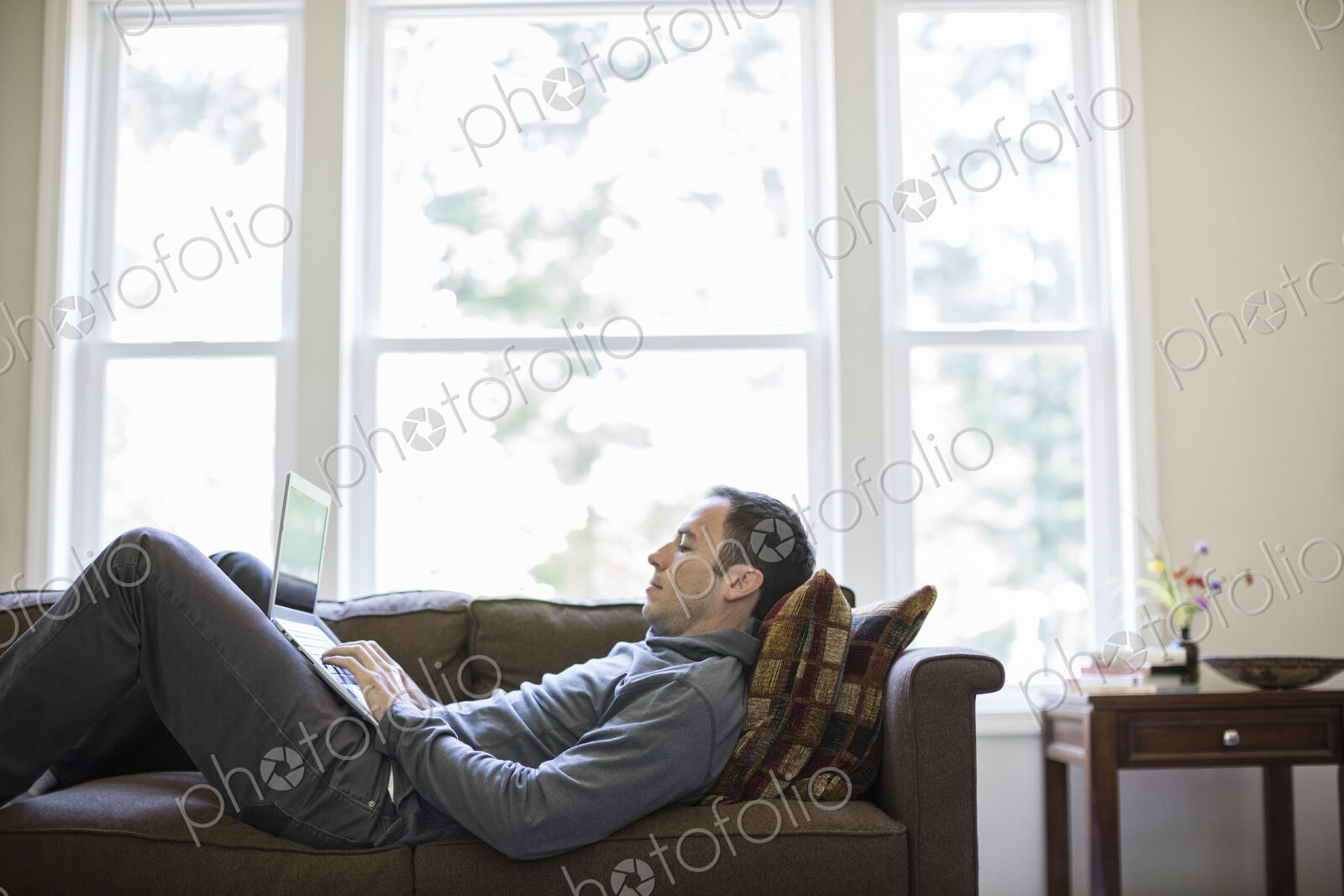 Caucasian man working on a laptop while on a couch in his home.
