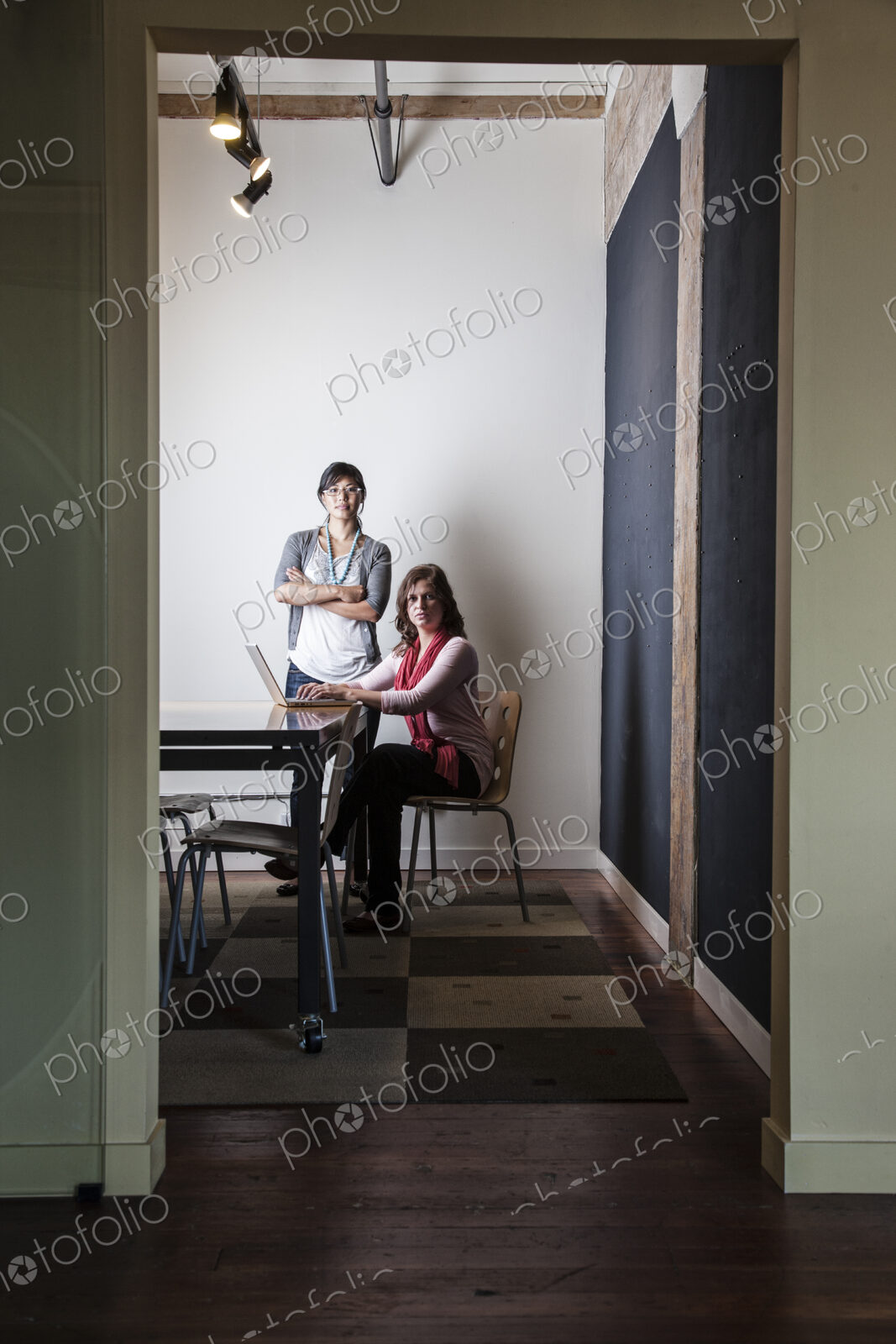 Caucasian woman and Asian woman working on a laptop computer in a small conference room.