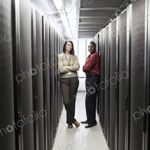 Caucasian woman and black man technician team in an aisle of a computer server farm. Caucasian woman and black man technician team in an aisle of a computer server farm.