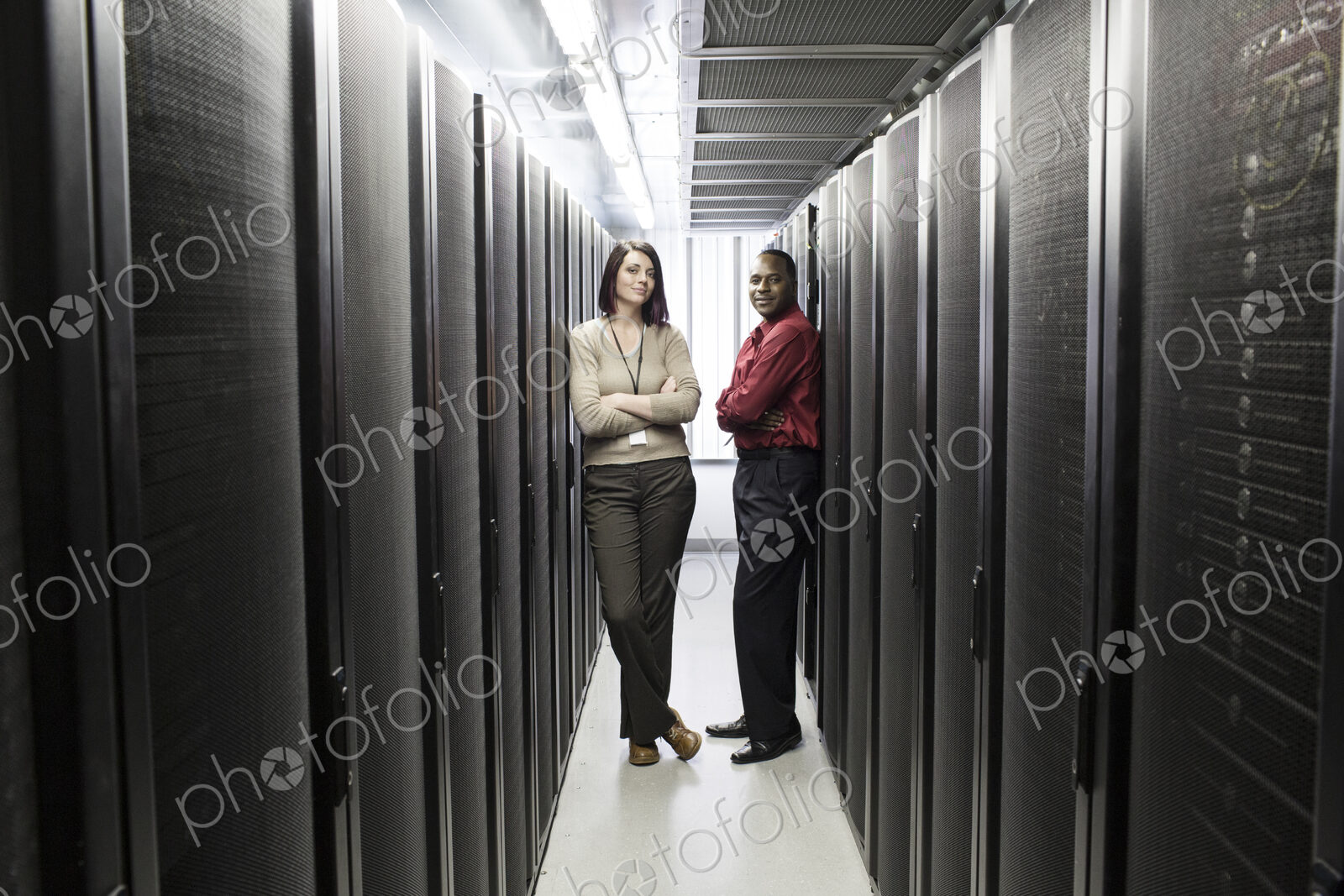 Caucasian woman and black man technician team in an aisle of a computer server farm.