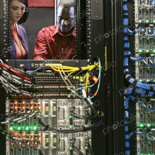 Caucasian woman and black man technicians running diagnostic tests on servers in a… Caucasian woman and black man technicians running diagnostic tests on servers in a…