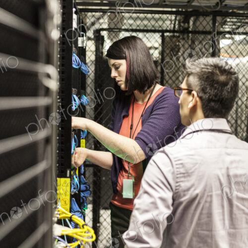 Caucasian woman and man technicians working on CAT 5 cables in a large computer server…