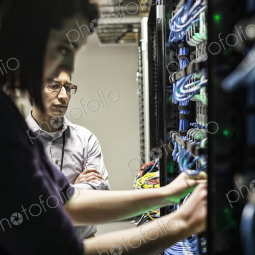 Caucasian woman and man technicians working on CAT 5 cables in a large computer server…