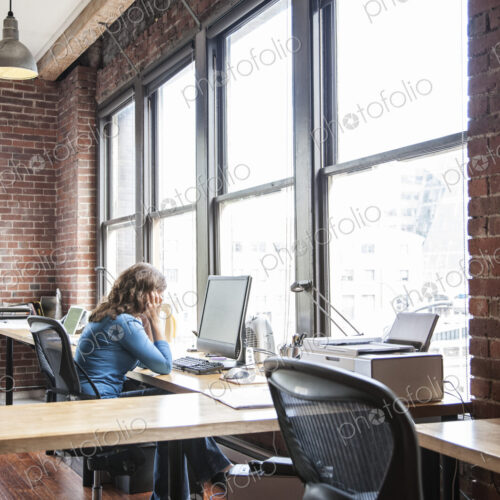 Caucasian woman at office workstation near a large bank of windows. Caucasian woman at office workstation near a large bank of windows.