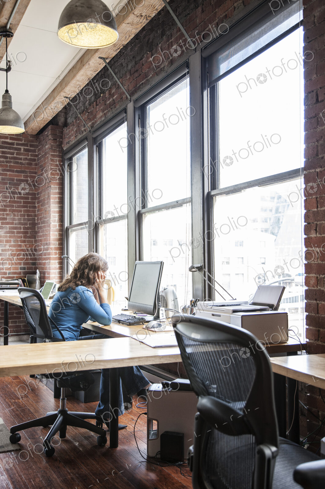 Caucasian woman at office workstation near a large bank of windows.