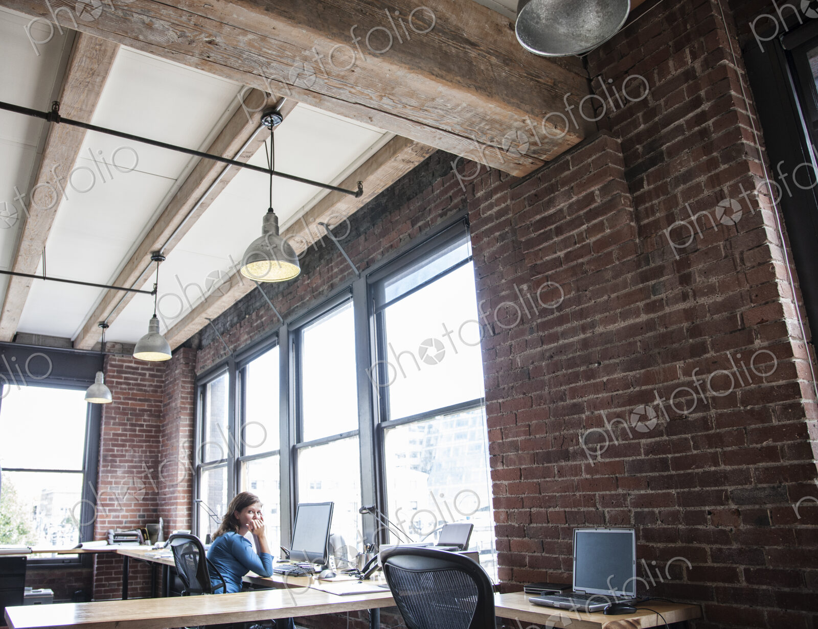 Caucasian woman at office workstation near a large bank of windows.