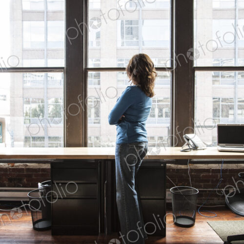 Caucasian woman at office workstation near a large bank of windows.