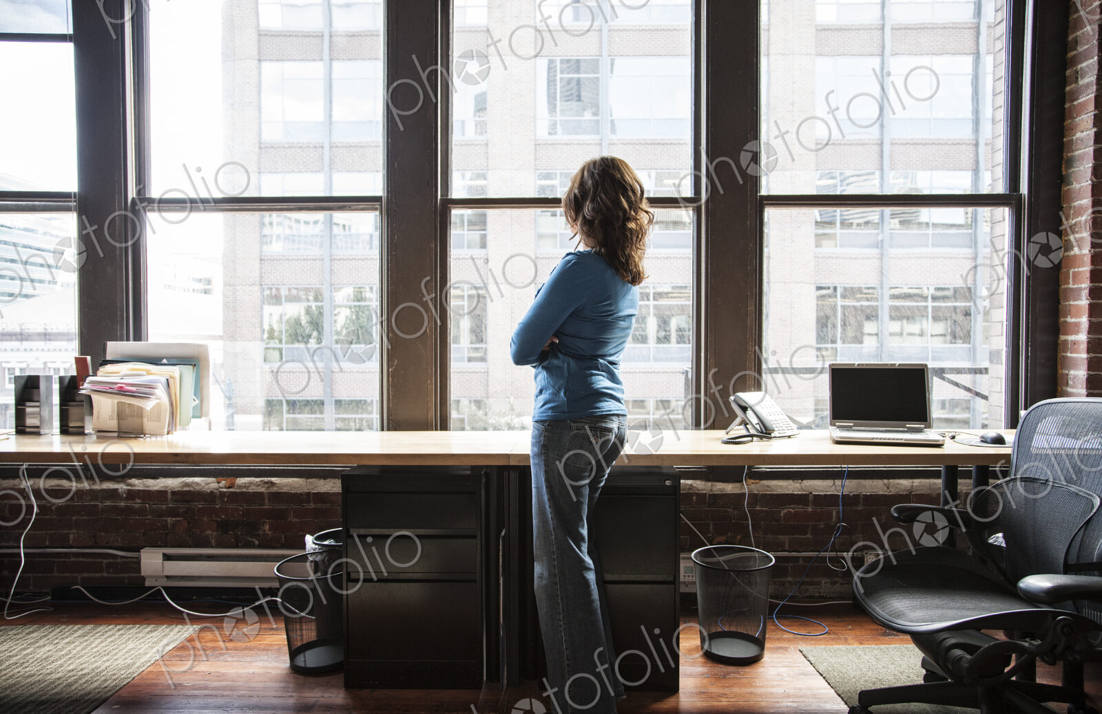 Caucasian woman at office workstation near a large bank of windows.