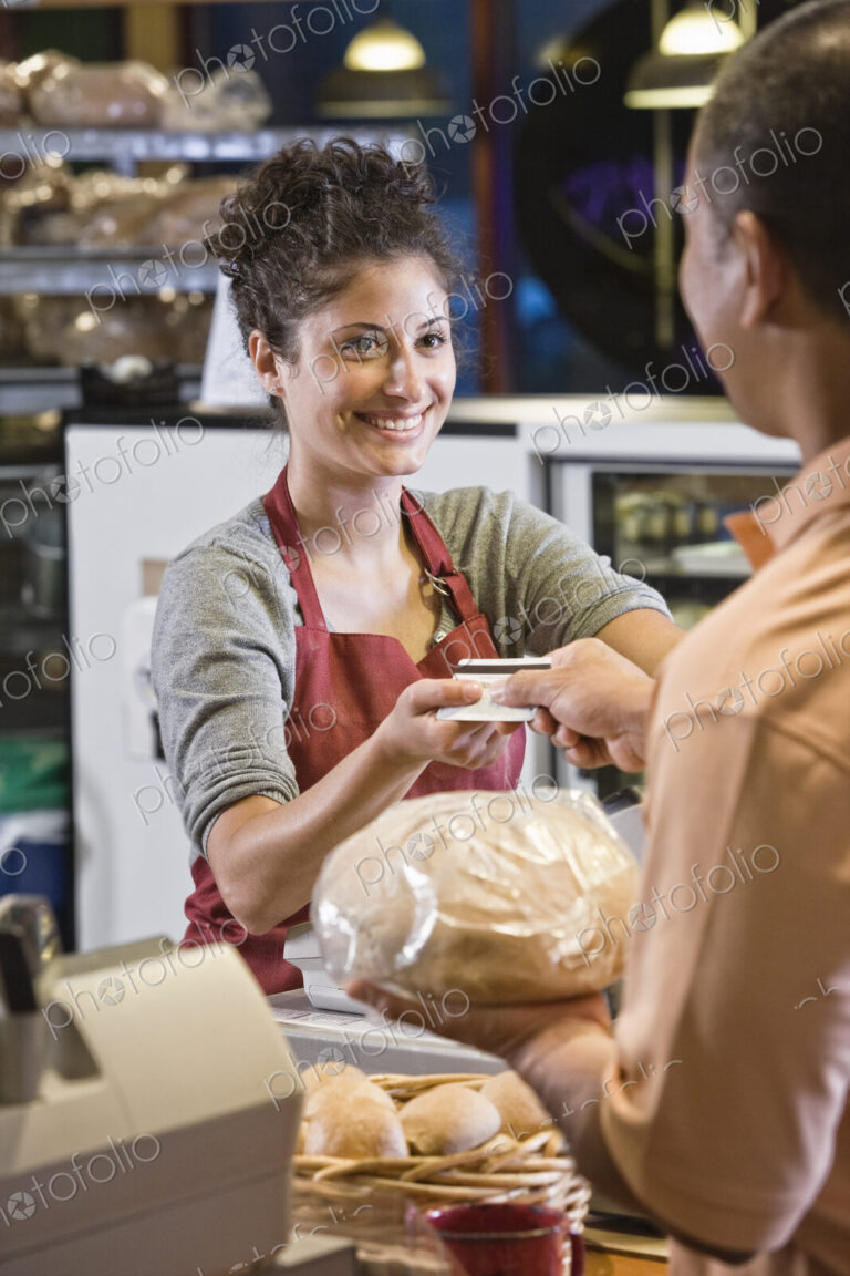 Caucasian woman at the cash register of a bakery making a credit card transaction with…