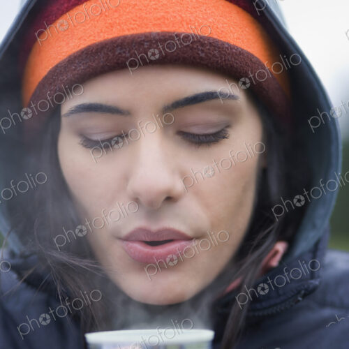 Caucasian woman blowing on the surface of a hot cup of coffee on a winter day. Caucasian woman blowing on the surface of a hot cup of coffee on a winter day.