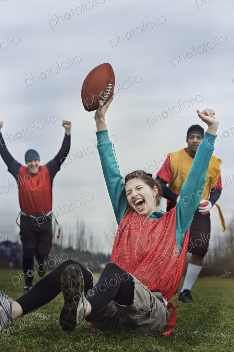 Caucasian woman celebrating with arms raised, scoring points in the end zone, in a…