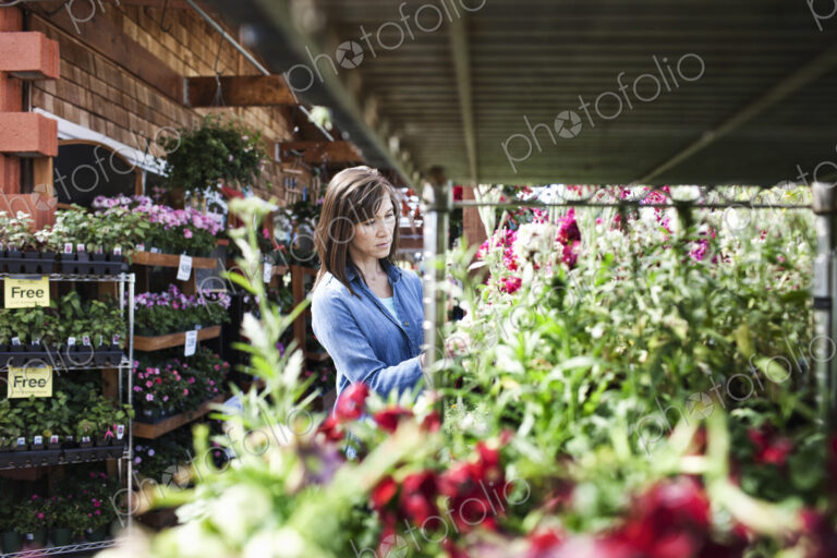 Caucasian woman checking on plants in a garden center nursery.