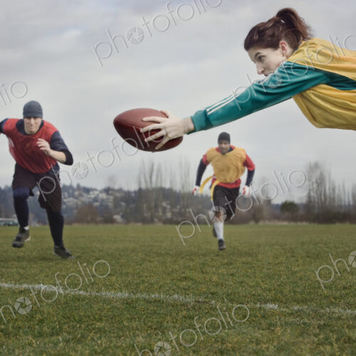 Caucasian woman diving with a football during a non-contact flag football match. Caucasian woman diving with a football during a non-contact flag football match.