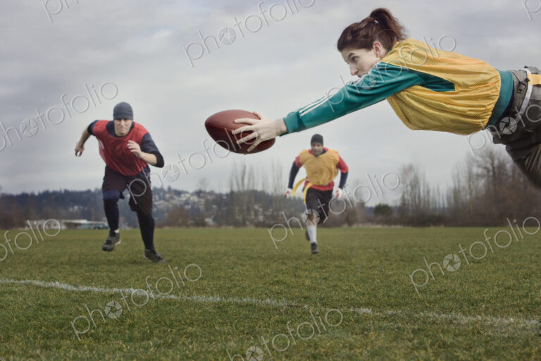 Caucasian woman diving with a football during a non-contact flag football match.