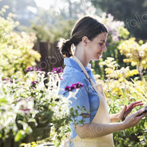 Caucasian woman employee of a garden center nursery texting in an order for new plants. Caucasian woman employee of a garden center nursery texting in an order for new plants.