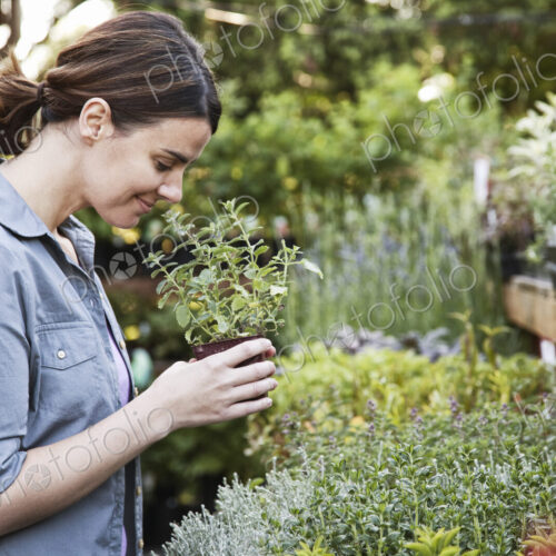 Caucasian woman holding a small plant, an aromatic herb and smelling it, shopping at a…