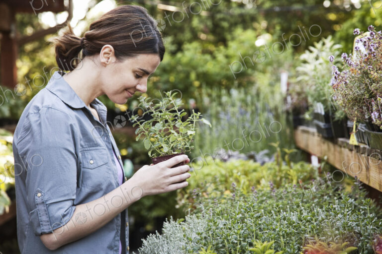 Caucasian woman holding a small plant, an aromatic herb and smelling it, shopping at a…
