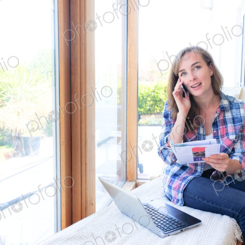 Caucasian woman holding paperwork and talking on cell phone near window Caucasian woman holding paperwork and talking on cell phone near window