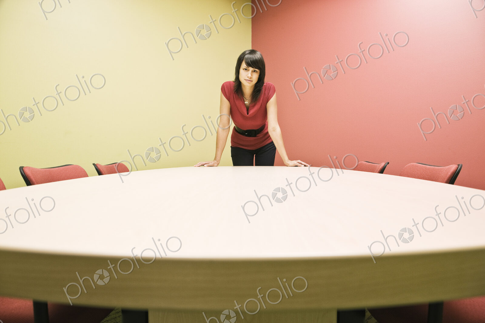 Caucasian woman in a conference room standing leaning on a table, confident pose.