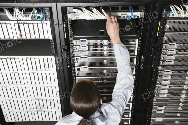 Caucasian woman lab technician working on servers in a computer sever farm.
