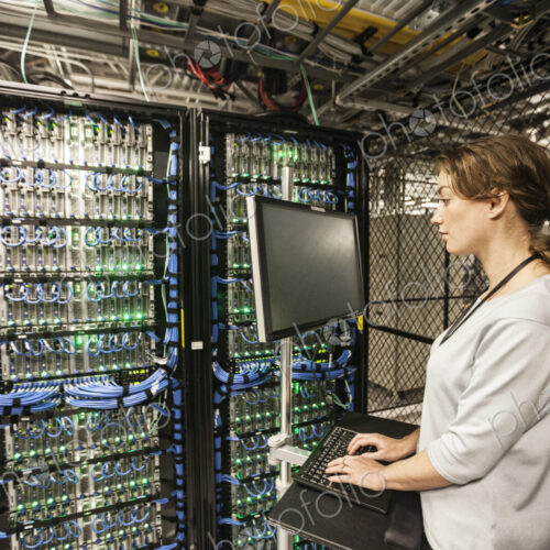 Caucasian woman technician doing diagnostic tests on computer servers in a server farm.