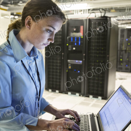Caucasian woman technician running diagnostics on computer servers in a server farm. Caucasian woman technician running diagnostics on computer servers in a server farm.