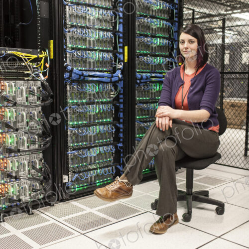 Caucasian woman technician sitting in an aisle of a large computer server farm. Caucasian woman technician sitting in an aisle of a large computer server farm.
