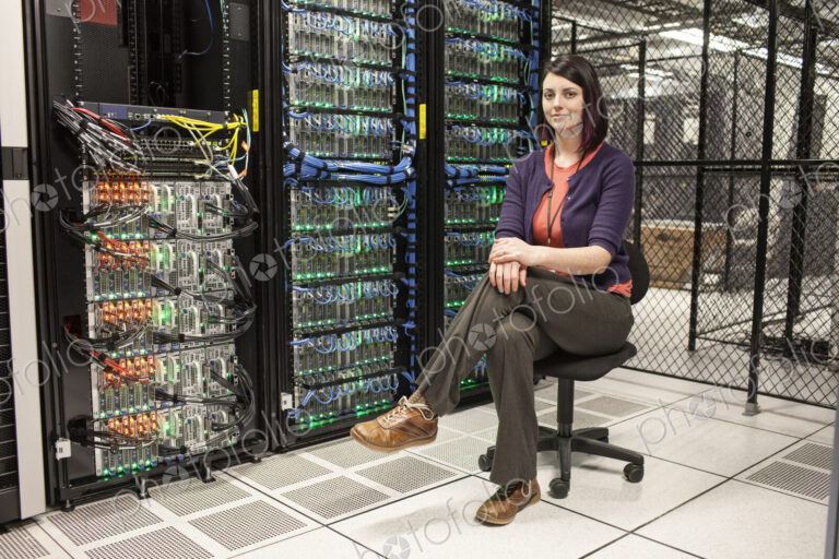 Caucasian woman technician sitting in an aisle of a large computer server farm.