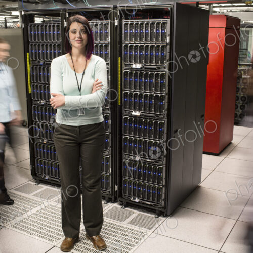 Caucasian woman technician standing in an aisle of a large computer server farm.