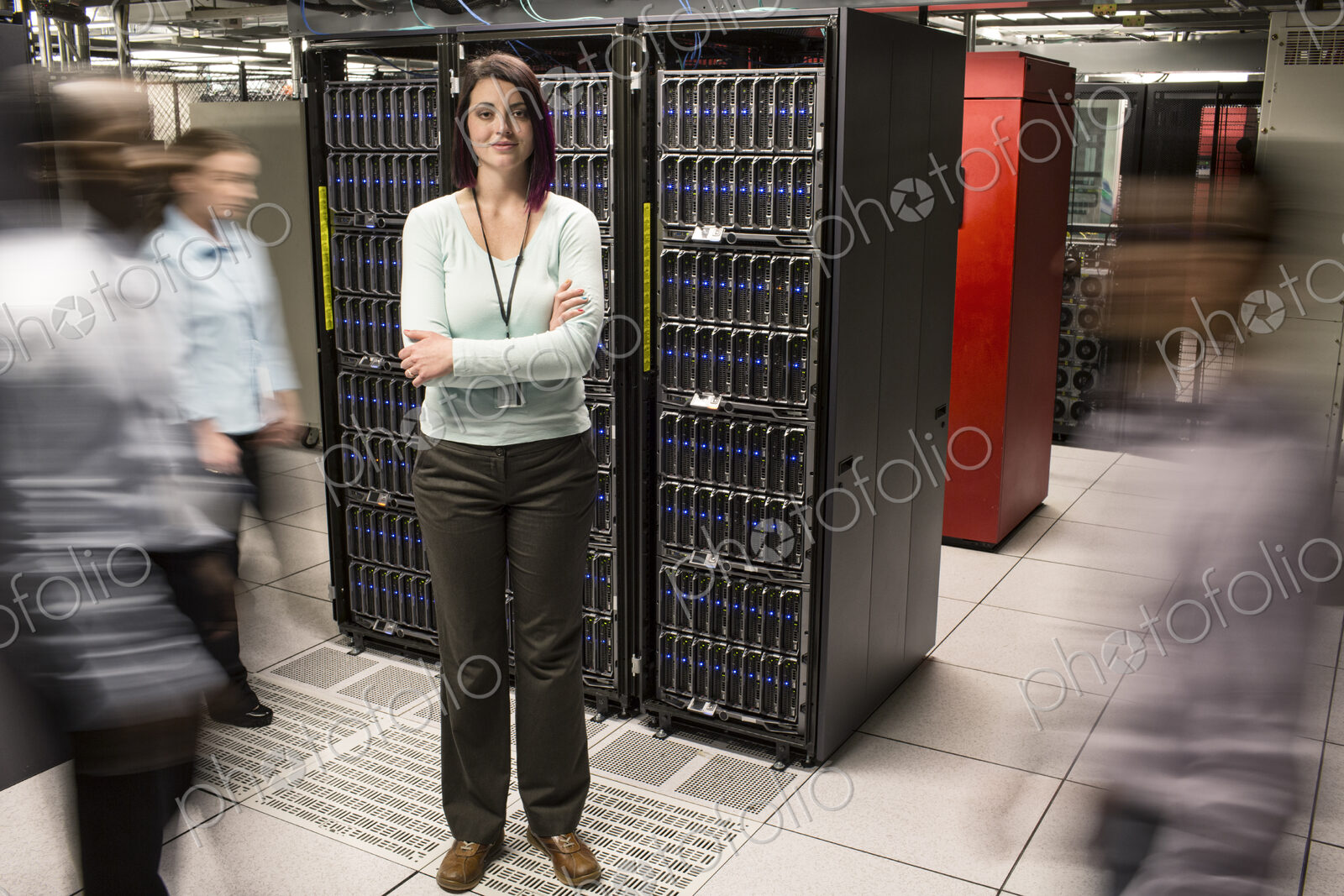 Caucasian woman technician standing in an aisle of a large computer server farm.