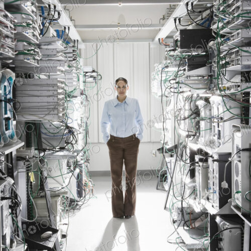Caucasian woman technician working in the aisle of a computer server farm. Caucasian woman technician working in the aisle of a computer server farm.